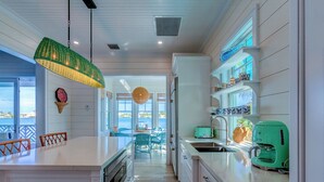 A kitchen with a central island, a dining area with chairs, and a view of the sea. - 3 bedroom Villa - Sunset Point, Abaco - Surf Inn Villa # 2 (Elbow cay)