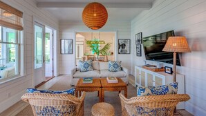 A living room with a sofa, wicker chairs, a coffee table, a TV, and a lamp. - 3 bedroom Villa - Sunset Point, Abaco - Surf Inn Villa # 2 (Elbow cay)