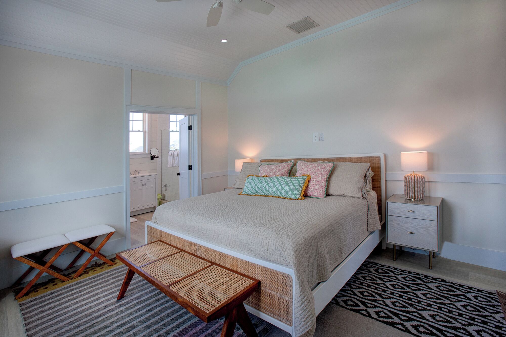 Une chambre à coucher avec un lit, des tables de chevet, un banc et un tapis à motifs.