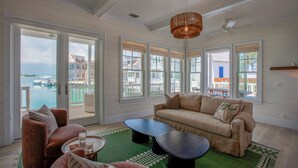 A spacious living room with a large sofa, a coffee table, and a view of the water and buildings outside. - South End Villa on the Water: Lovely Pool, Expansive Decks, and 60’ Private Dock (Elbow cay)