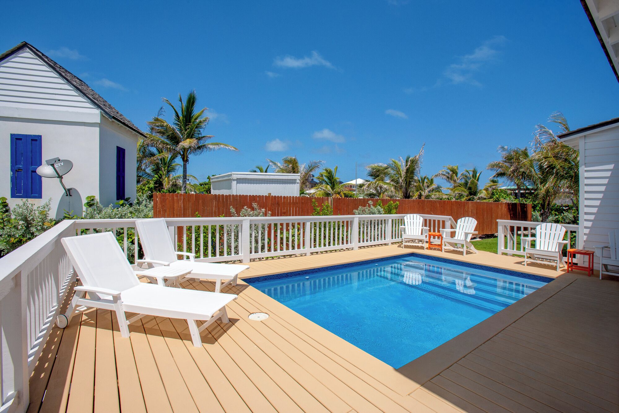 A backyard with a swimming pool, white deck chairs, and a wooden fence.
