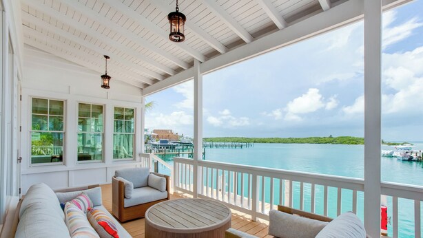A covered outdoor area with a view of the water, furnished with sofas and a round table. - South End Villa on the Water: Lovely Pool, Expansive Decks, and 60’ Private Dock (Elbow cay)