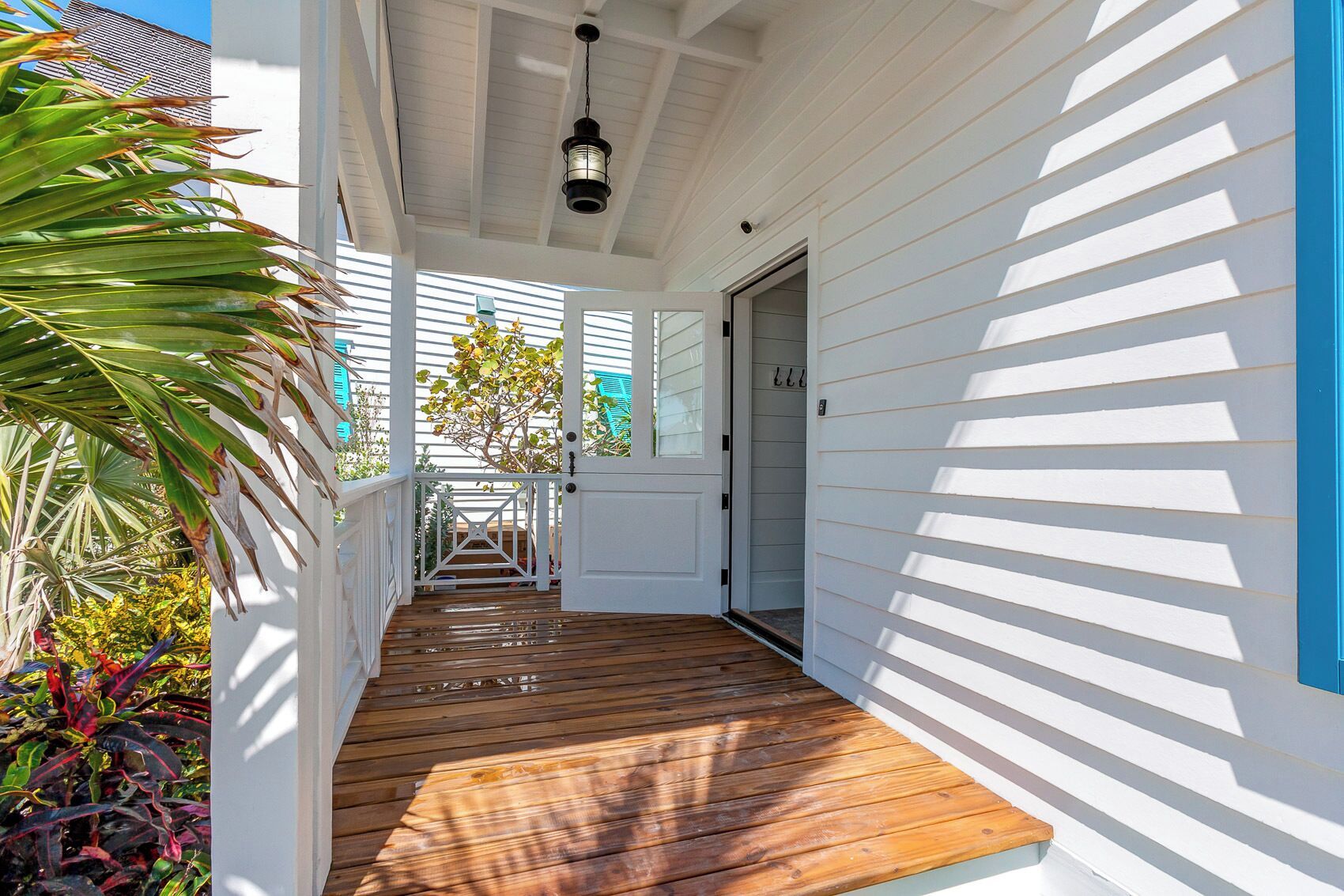 A wooden deck leading to a white door with a number sign, surrounded by lush tropical plants.