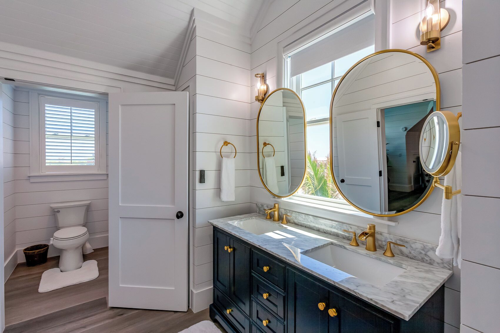 A bathroom with a white toilet, a vanity with a marble countertop, and two large mirrors with gold frames.