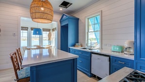 Una cocina con una isla central, armarios azules, lavavajillas y una ventana con contraventanas azules.