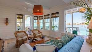Un amplio salón con muebles de mimbre, un ventanal con vistas al mar y un ventilador de techo.