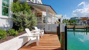 Eine Holzterrasse mit weißen Adirondack-Stühlen, einem überdachten Sitzbereich und Blick auf ein klares, blaues Schwimmbecken.
