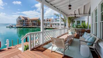 A wooden deck with outdoor furniture, a white railing, and a view of a marina with boats and houses.