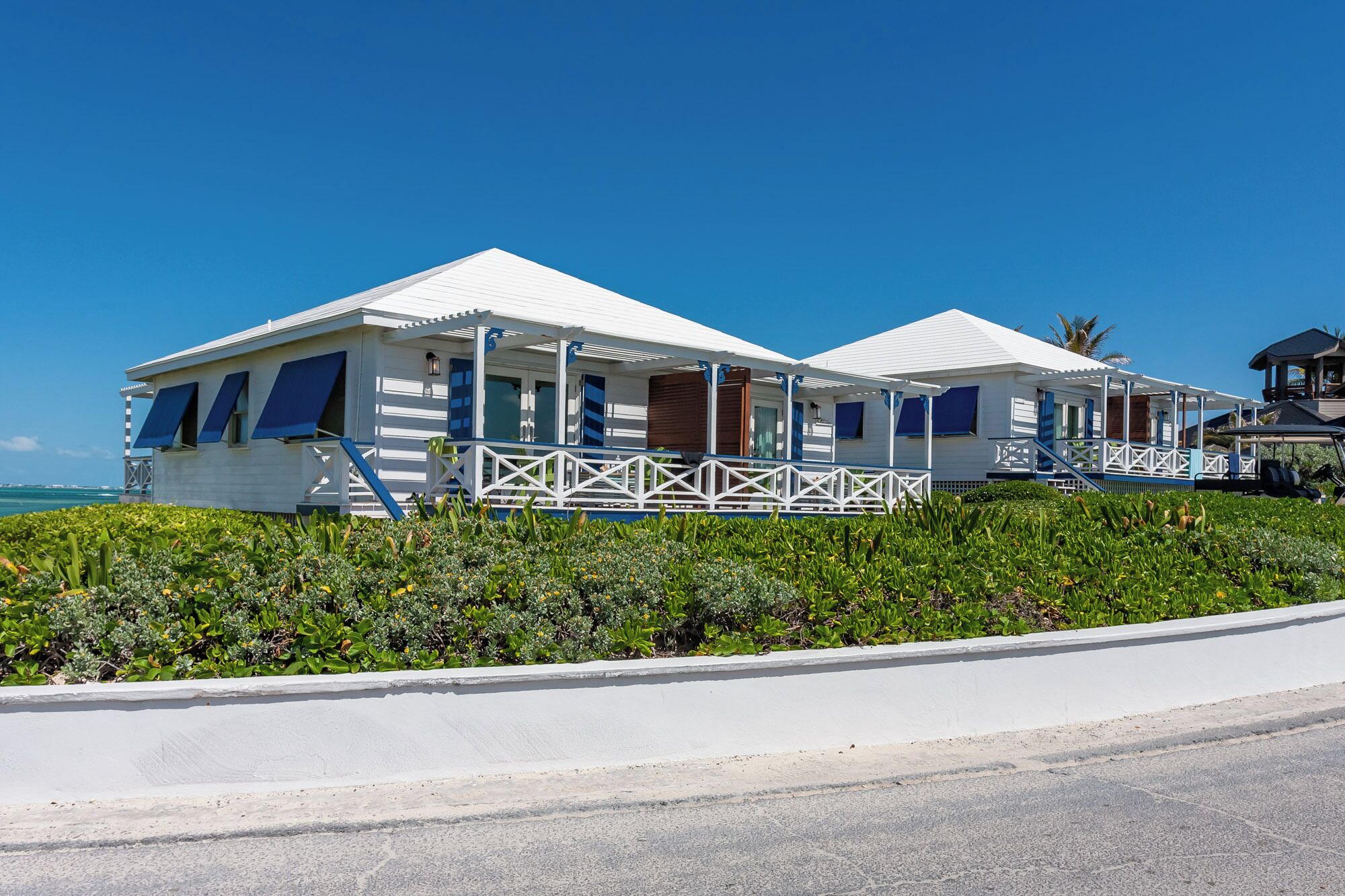 A beachfront hotel with white and blue structures, a covered walkway, and a view of the ocean.
