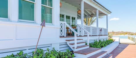 A white building with a covered porch, steps leading to the porch, and a wooden deck.