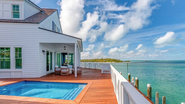 Une maison blanche avec une terrasse en bois, une piscine et une vue sur l’océan.