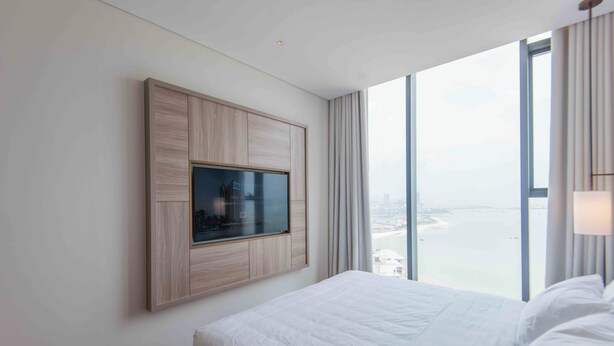Une chambre d’hôtel moderne dotée d’un grand lit, d’un téléviseur fixé au mur et offrant une vue sur la ville grâce à de grandes fenêtres.