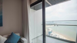 Un salon moderne avec un balcon en verre donnant sur une plage et offrant une vue sur la ville.