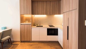 Une cuisine compacte dotée de meubles en bois, d’un évier, d’un four à micro-ondes et d’un coin repas avec une chaise.