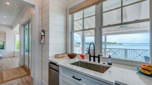 A modern kitchen with a large window overlooking a marina, white cabinetry, and a stainless steel sink.