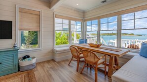 A spacious room with a large window offering a view of the water and boats, a wooden dining table with chairs, and a cozy seating area.