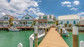A waterfront property with multiple docked boats, a wooden pier leading to the dock, and several white buildings with green shutters.