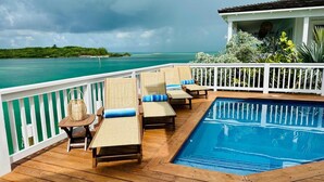 Een houten terras met een zwembad, ligstoelen en uitzicht op zee.