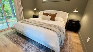 Un dormitorio moderno con una cama grande, vistas a espacios verdes a través de una ventana y dos lámparas de noche.