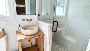 Un baño con lavamanos redondo, un espejo, ducha con puertas de vidrio y suelo de baldosas.