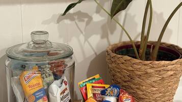 A glass jar with snacks, a bowl of assorted chocolates, and a potted plant on a wooden tray.