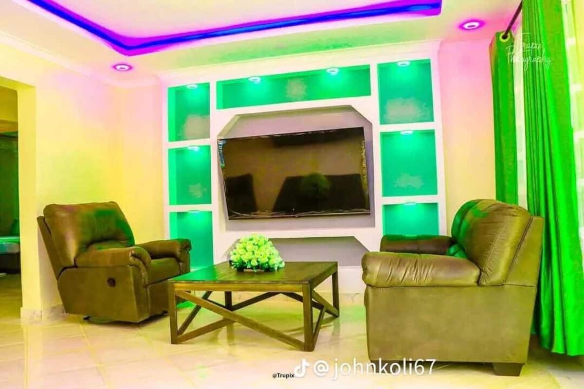 A living room with two leather sofas, a coffee table, and a flat-screen TV mounted on a wall with green lighting.