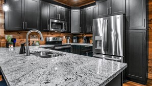 A modern kitchen with dark cabinets, stainless steel appliances, granite countertops, and wooden ceiling accents. - Pearl's Mountain Retreat: Wifi, Hot Tub, Free Attraction Tickets, & Game Room (Sevierville)