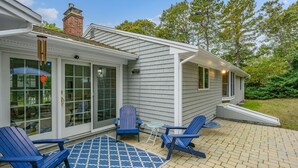 Una casa con patio coperto, arredato con poltrone Adirondack blu e un tappeto decorato.