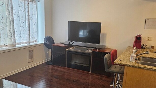 A living room with a flat-screen TV, a coffee maker, and a dining area with a kitchen counter.