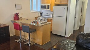 A compact living space with a kitchenette, a dining area with bar stools, a leather sofa, and a glass-top coffee table.