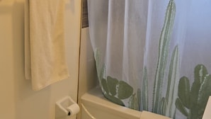 A bathroom with a shower curtain featuring a cactus design, a toilet, and a bathtub with a towel on it.