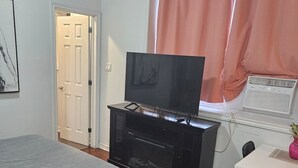 Een slaapkamer met een bed, een televisie op een standaard, een raam met gordijnen en een deur.