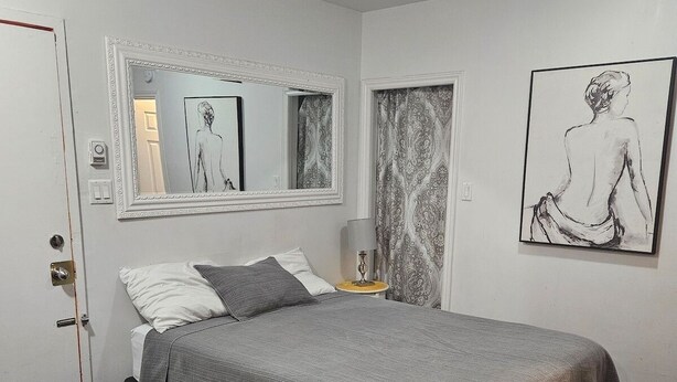 Een slaapkamer met een bed, een spiegel, een schilderij en een deur.