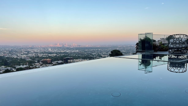 A rooftop infinity pool with a cityscape view, a glass railing, and a decorative planter. - Serene Detached Glass Studio—Common Areas with Iconic LA Skyline Views (Los Angeles)