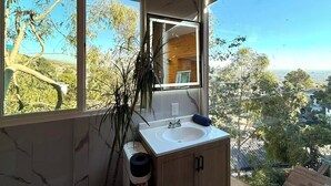 A bathroom with a large window, a sink, and a mirror. - Serene Detached Glass Studio—Common Areas with Iconic LA Skyline Views (Los Angeles)