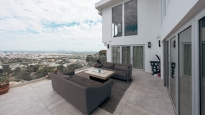 A modern outdoor living area with a sofa and coffee table, a view of the city, and a large window. - Serene Detached Glass Studio—Common Areas with Iconic LA Skyline Views (Los Angeles)