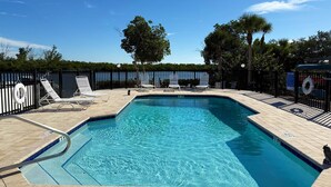 A rectangular swimming pool with a tiled deck, surrounded by black metal railings and white lounge chairs. - Sea Oats by the Bay – Pool, Beach & Boat Slips (Englewood)