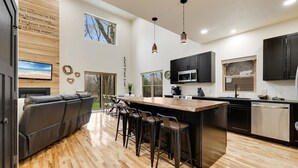 A modern kitchen with a central island, bar stools, and a dining area with a sofa.