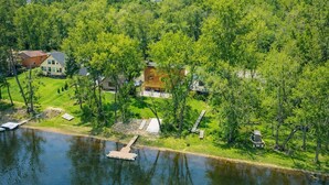 An aerial view of a lakeside property with a dock, a gazebo, and several houses surrounded by dense greenery.