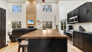 A modern kitchen with a central island, black cabinets, and a wooden countertop.
