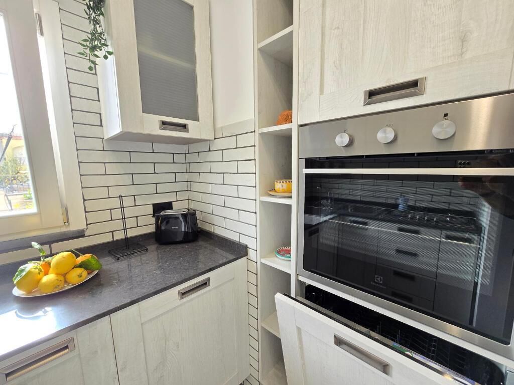 A modern kitchen with white cabinets, a black countertop, and a built-in oven.