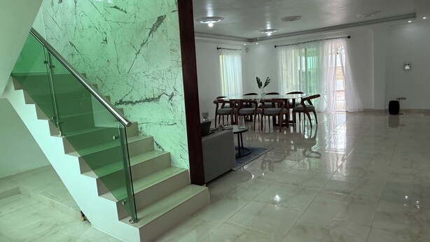 A spacious, well-lit room with a marble staircase, a dining area with a table and chairs, and large windows allowing natural light. - Modern Getaway with Private Pool, Montecristi (villa vasquez)