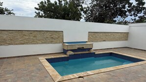 A rectangular swimming pool with a stone border and steps leading into it, surrounded by a tiled patio and a white wall with stone accents. - Modern Getaway with Private Pool, Montecristi (villa vasquez)