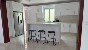 A modern kitchen with white cabinets, a marble countertop, and three black bar stools. - Modern Getaway with Private Pool, Montecristi (villa vasquez)