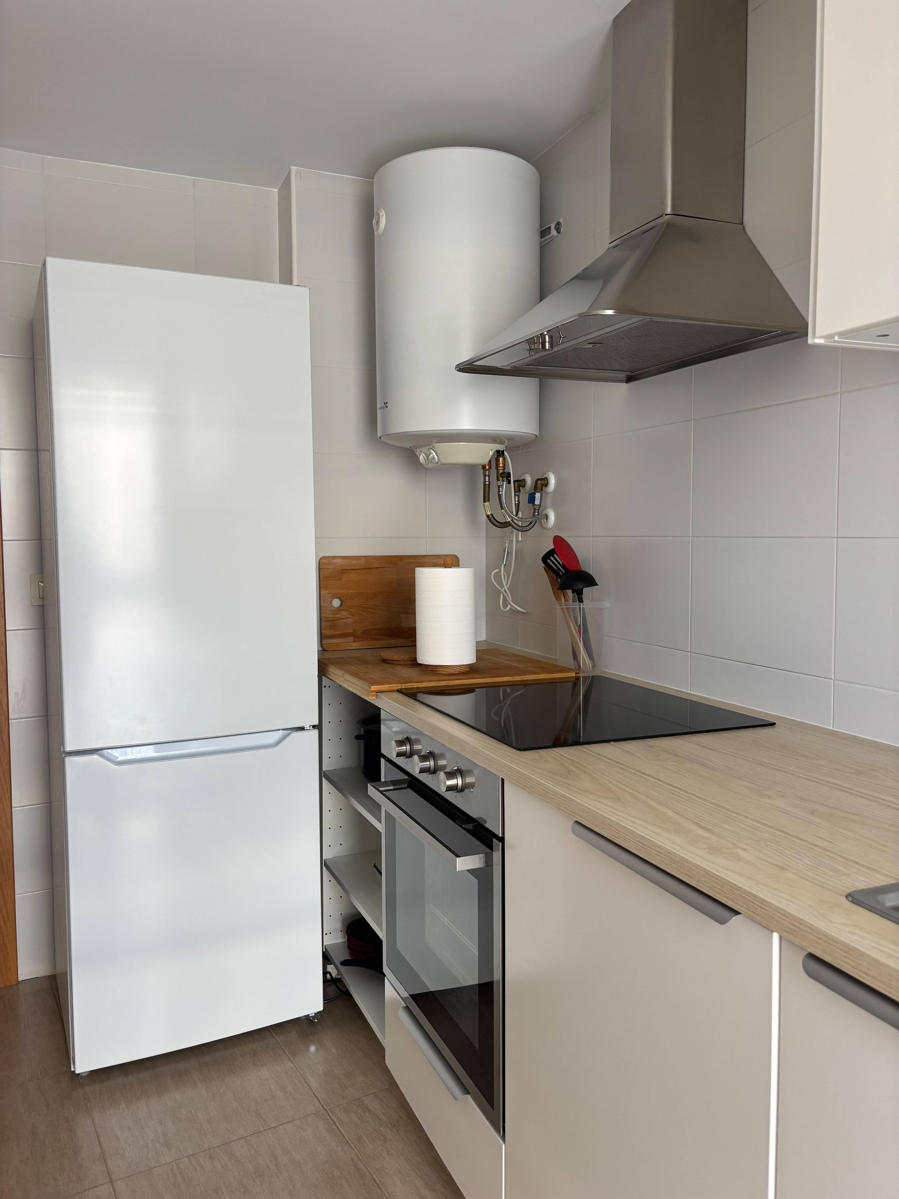 Una cucina moderna con frigorifero bianco, forno a incasso, piano cottura e un piano di lavoro in legno.