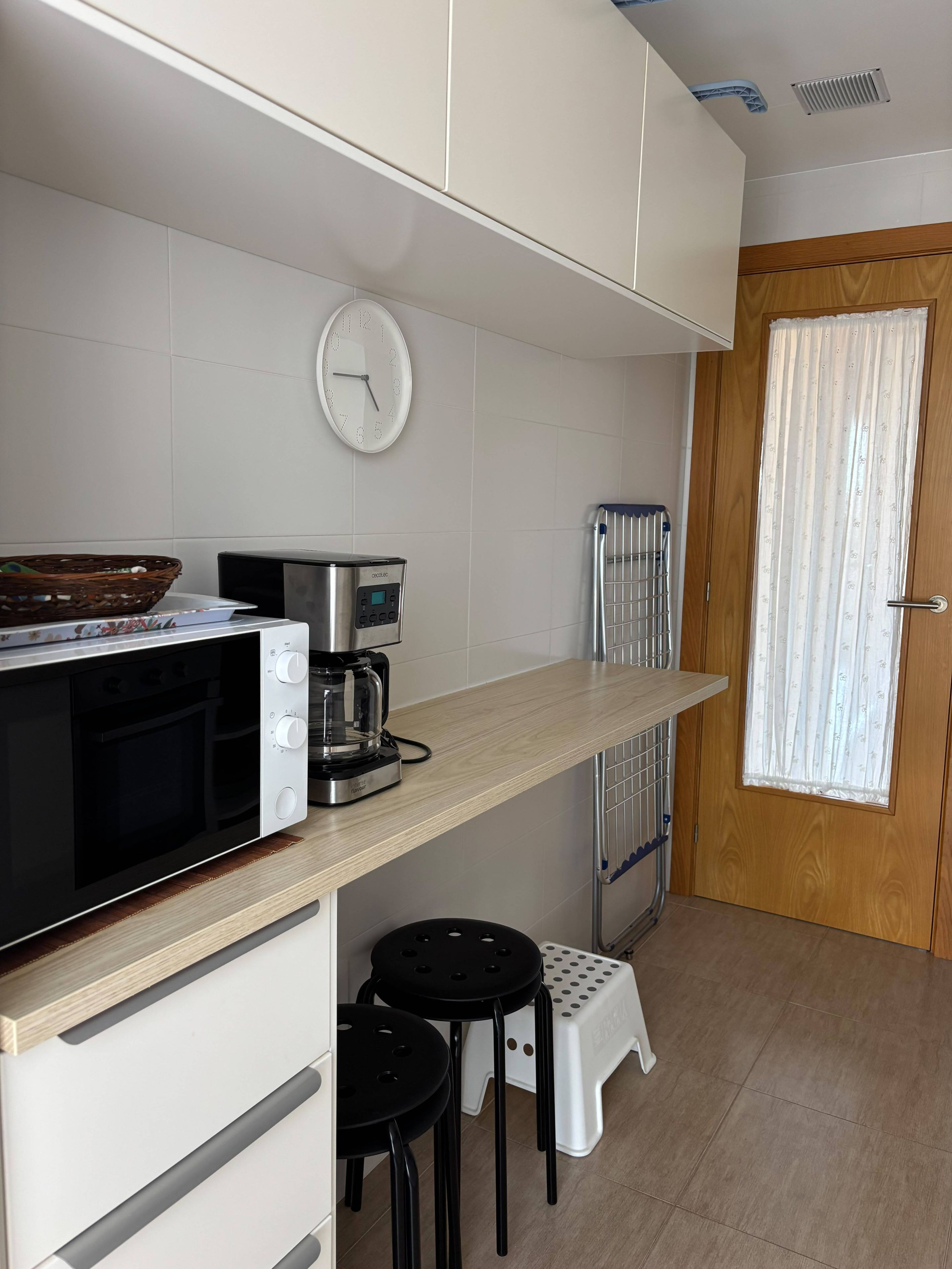Una kitchenette compacta con microondas, cafetera y refrigerador pequeño.