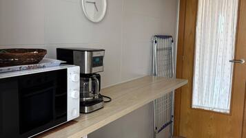 Una kitchenette compacta con microondas, cafetera y refrigerador pequeño.