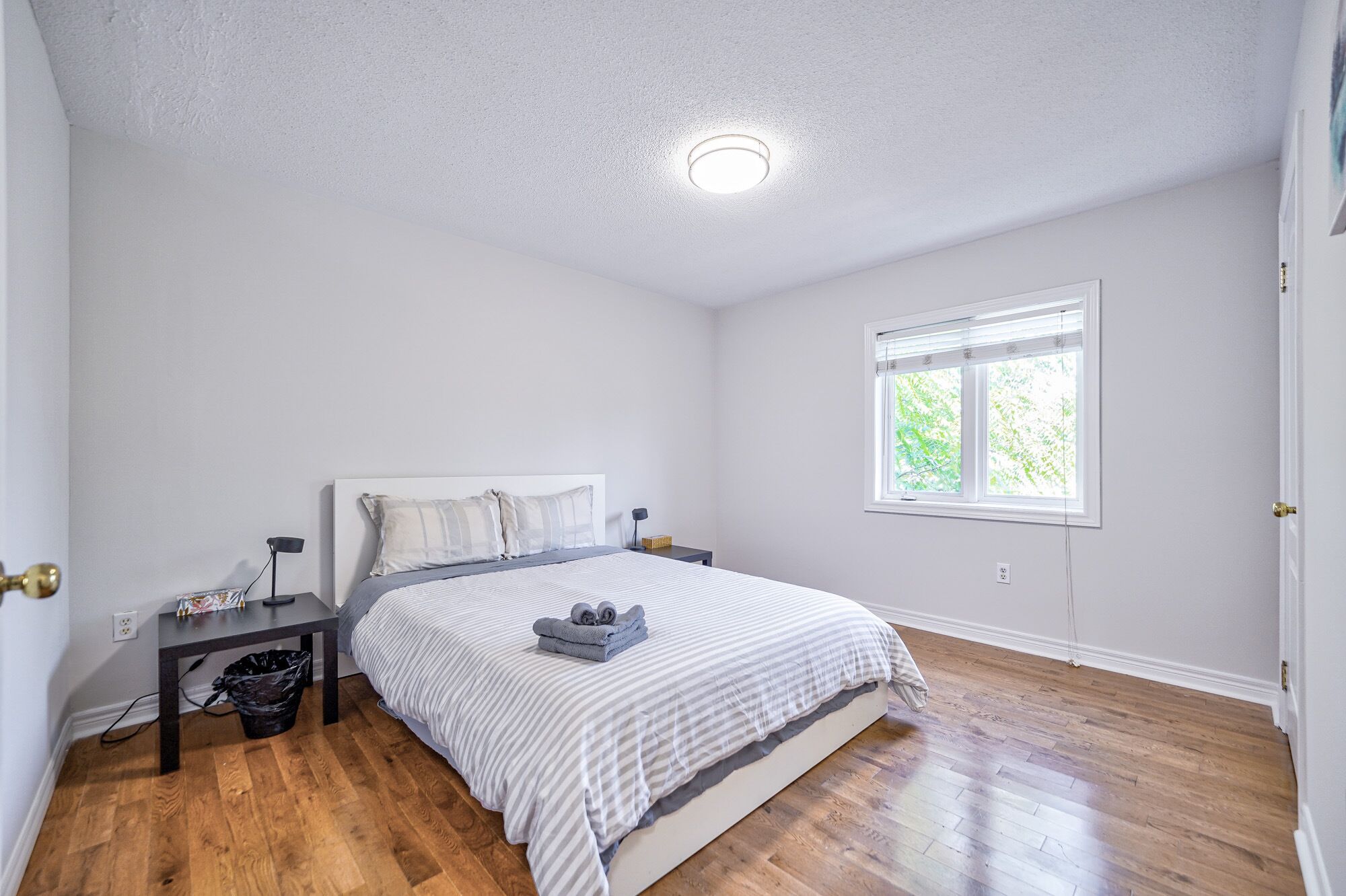 A bedroom with a bed, a nightstand, a window, and a ceiling light.
