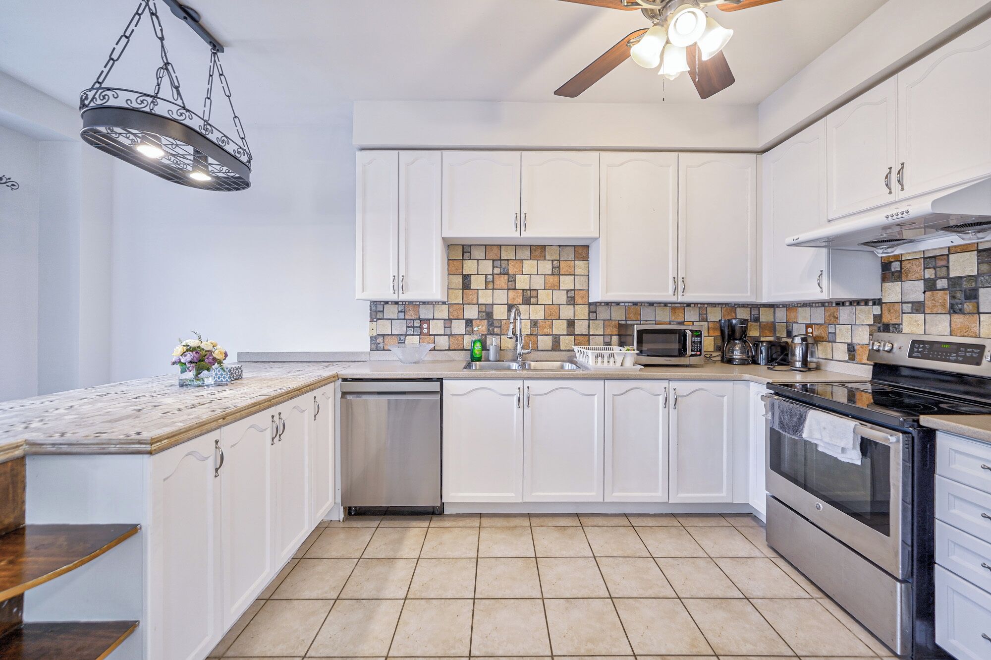 A modern kitchen with white cabinets, a tiled backsplash, stainless steel appliances, and a ceiling fan.