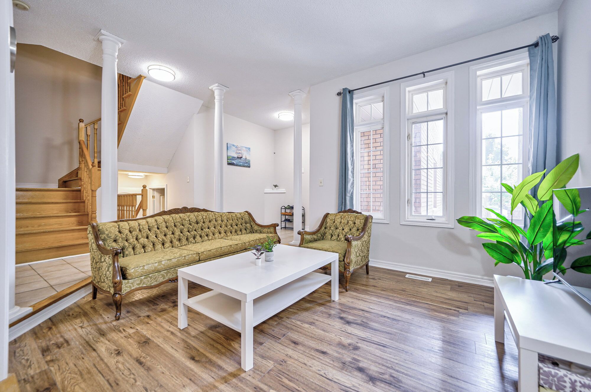 Un salon avec un canapé vert, une table basse blanche et un escalier.